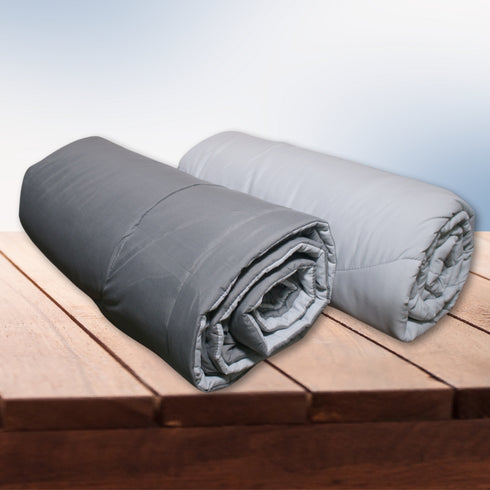 Two rolled-up reversible comforters, one gray and one white, placed on a wooden surface.