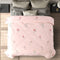 A pink comforter with a floral pattern on a single bed in a room with various bedding and decor.