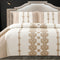 A king-size bed with a white and gold quilted bed cover and two pillow covers with a similar design.