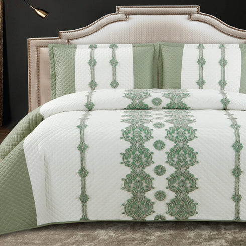 A king-size bed with a green and white quilted bed cover and two pillow covers with a floral pattern.