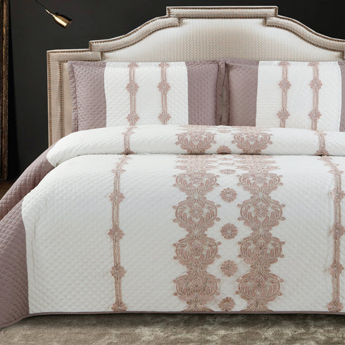 A king-size bed with a white and pink quilted bed cover featuring a floral lace pattern, accompanied by two pillow covers with the same design.