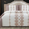 A king-size bed with a white and pink quilted bed cover featuring a floral lace pattern, accompanied by two pillow covers with the same design.