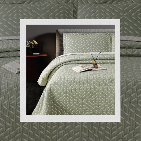 A bed covered with a green jacquard bedcover set with a geometric pattern, along with two pillow covers, on a bed in a room setting.