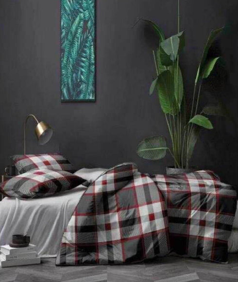 A checkered patterned top sheet displayed on a bed in a bedroom setting, with a variety of colors including red, black, and gray.