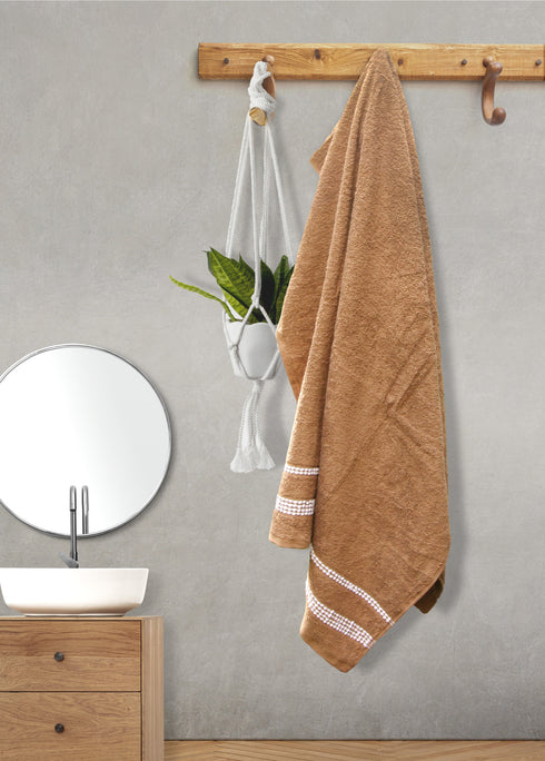 Brown towel with white trim hanging on a wooden towel rack in a bathroom.
