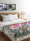 A double bed with a floral print blanket and white sheets, with a wooden headboard and a bedside lamp in the background.