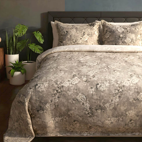 Floral patterned comforter on a bed with decorative pillows and plants in the background.