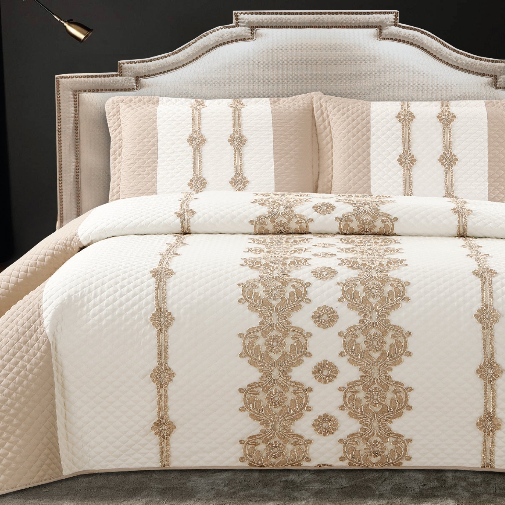 A king-size bed with a white and gold quilted bed cover and two pillow covers with a similar design.
