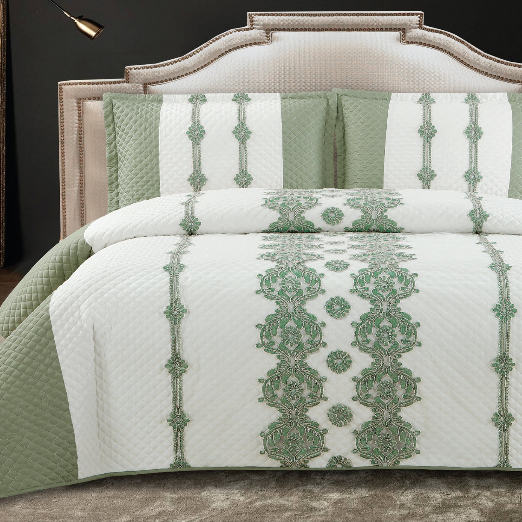 A king-size bed with a green and white quilted bed cover and two pillow covers with a floral pattern.