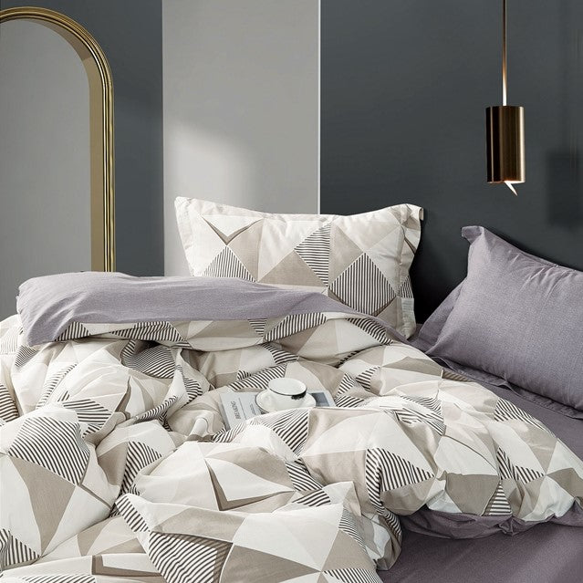 A king-size bed with a white and geometric patterned bedsheet set and two pillow covers, placed against a dark wall with a modern hanging light and mirror.