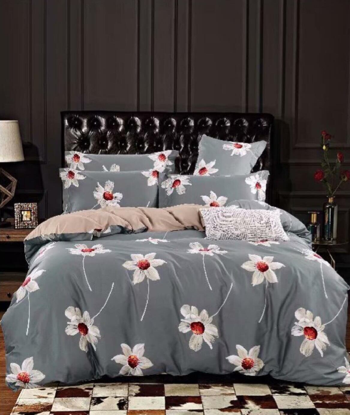 A floral printed top sheet displayed on a bed with a dark headboard, the sheet has a grey base with red and white flower designs.